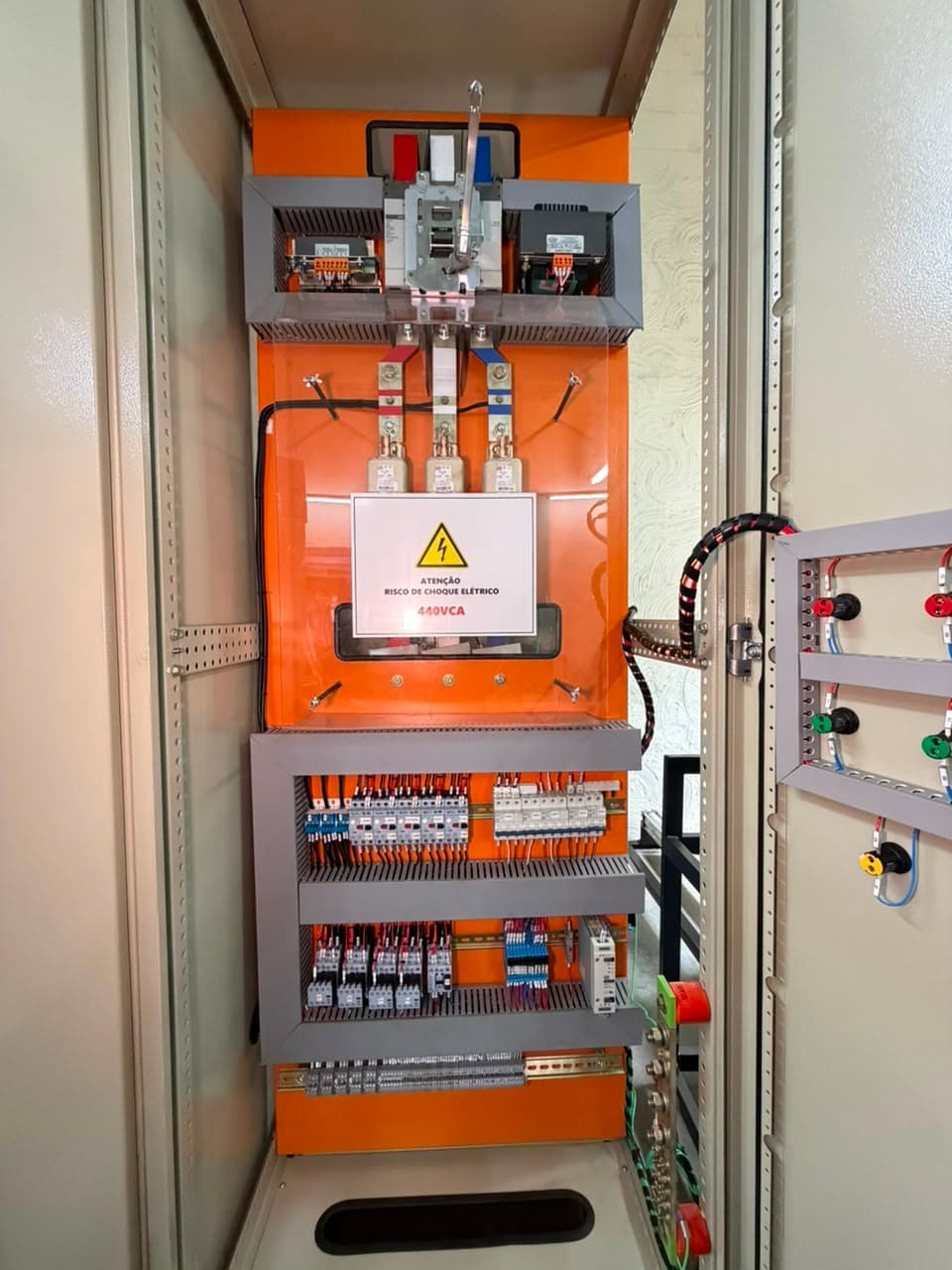 Painel aberto com seccionadora, fusíveis sob proteção transparente e aviso de risco de choque elétrico de 440 volts